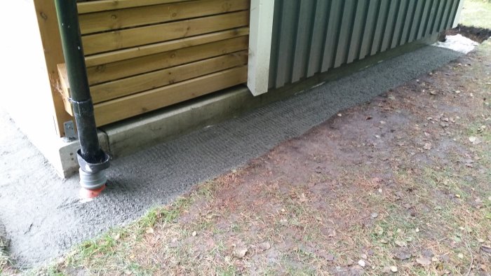 Nyinstallerade trottoarplattor bredvid träfriggebod, med synlig makadamkant och naturmark.