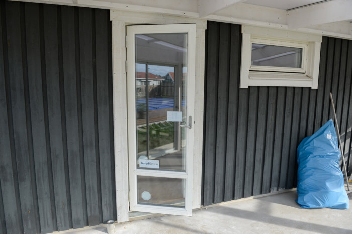 Glasdörr och fönster installerade på trähus med mörk panel och pågående byggarbete.
