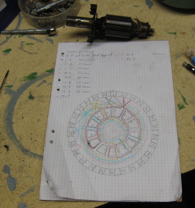 Lindningsschema ritat på rutat papper med flera färger, vid sidan av en demonterad motor och verktyg på ett arbetsbord.