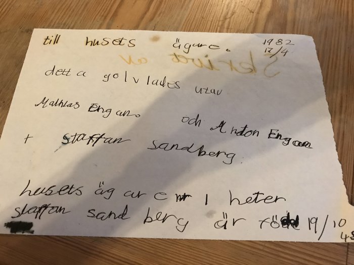 Ett gammalt handskrivet budskap upphittat under ett husgolv, daterat 1982, med personliga meddelanden och namn.