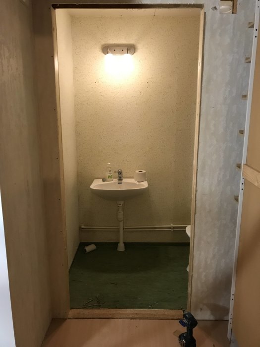 Orenoverat badrum med gammal inredning och grönt golv före renovering.