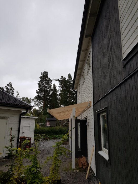 Delvis färdigställd träaltan under konstruktion på sidan av ett svart och vitt hus.