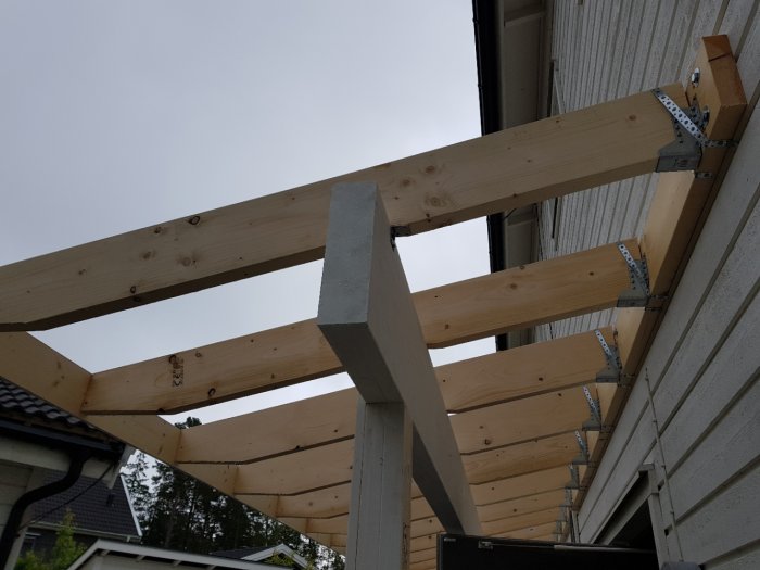 Konstruktion av träbjälkar och metallbeslag på ett byggprojekt nära en byggnad.