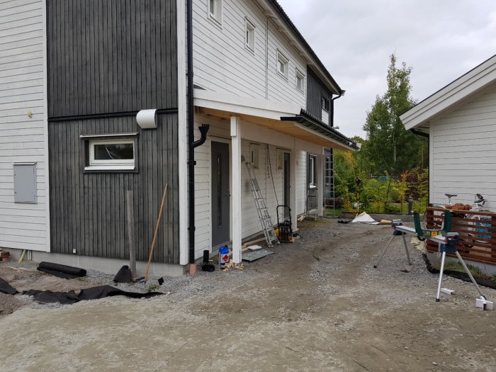 Vitt hus under renovering med grått, obrukat entréparti och byggmaterial spridda runt omkring.