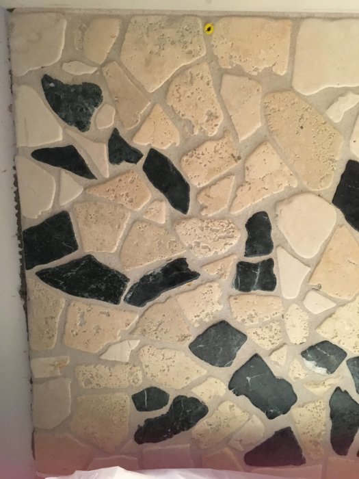 Olika storlekar av stenplattor i mosaikmönster monterade på en vägg.