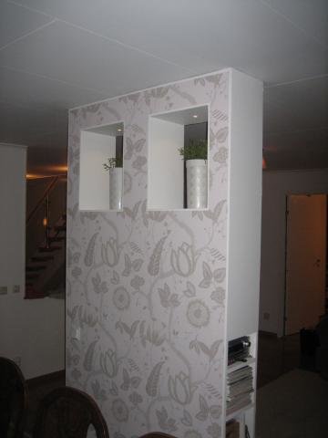 Decorative wall with floral wallpaper, featuring two shelves with plants and a hidden compartment for cables. Integrates LED lights and in-wall speakers.