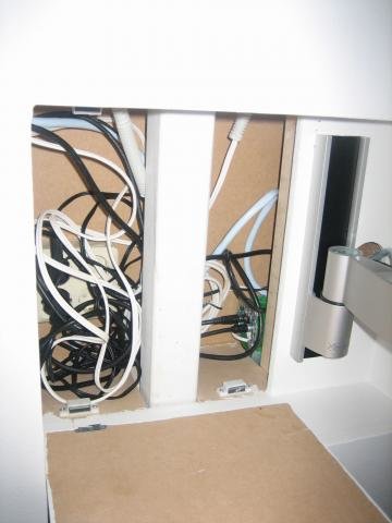 Cables and wires organized inside a wall compartment with an open panel, showing electrical and antenna connections for TV and stereo systems.