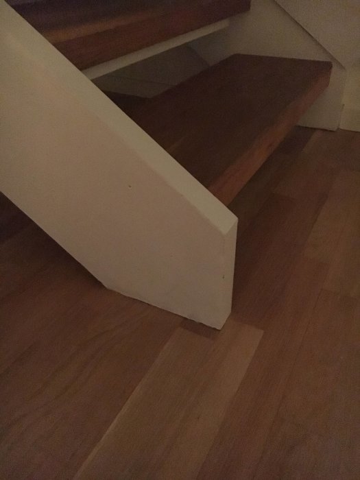 Två typer av parkettgolv med skiljande list vid en trappa i en bostad.