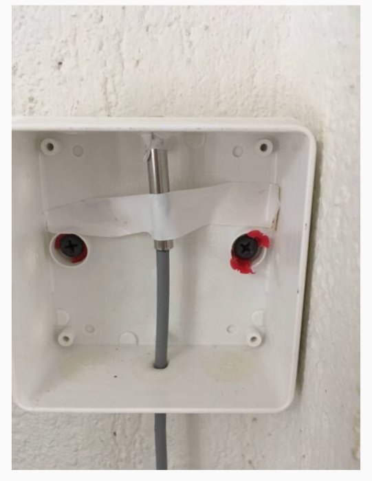 En öppen eldosa med en utstickande elkabel och tejpade ledningar i väggmontage.