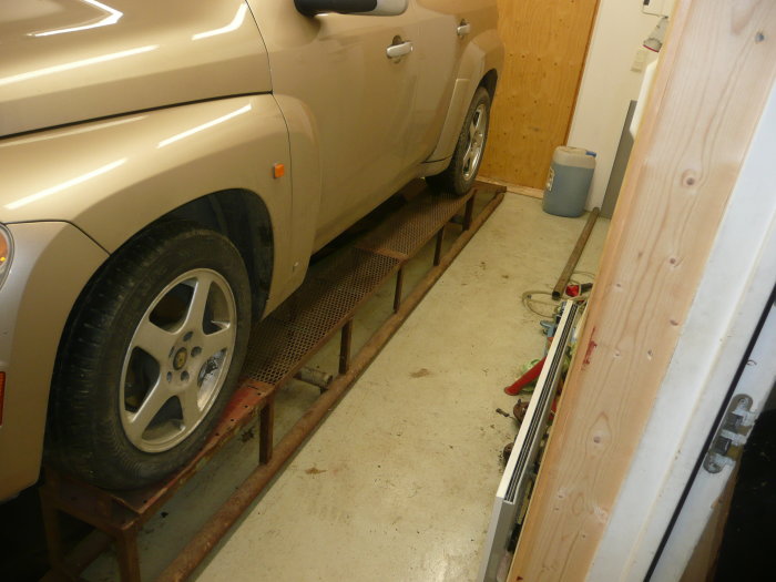 En bil parkerad på en improviserad ramp av stålrör och gallersteg i ett garage.
