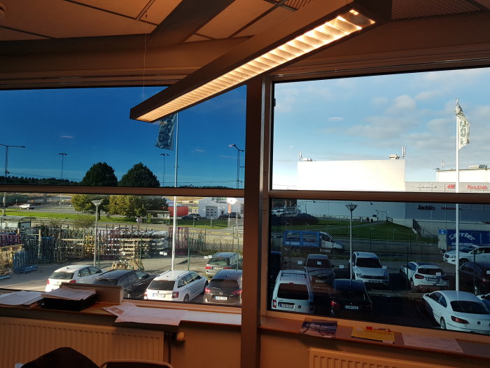 Utsikt från nyinstallerade fönster mot parkeringsplats och företagsbyggnader i dagsljus.