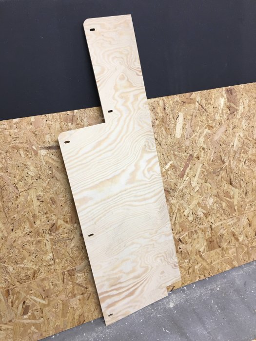 Fräsmall i furuplywood med hål för dominofogar, framför OSB-skiva och svart MDF-panel.