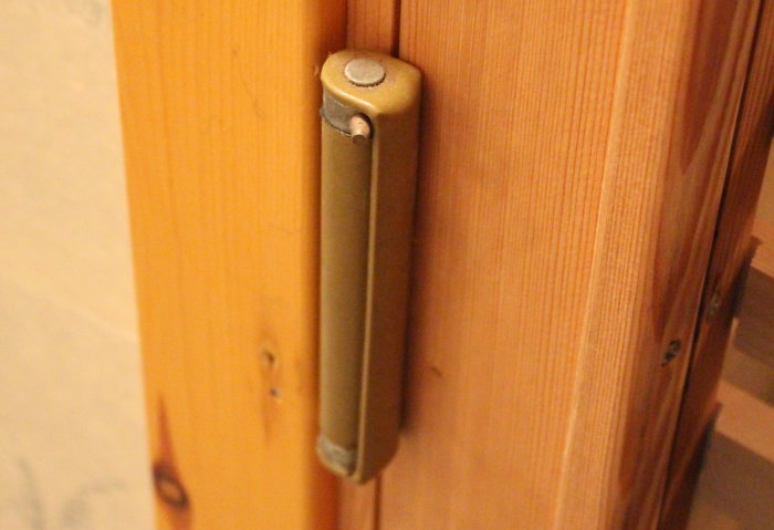 Ett dörrgångjärn med inbyggd stängningsfjäder monterat på en bastudörr i trä.