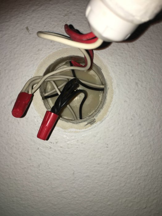 Takdosa med öppna elektriska anslutningar, inklusive röda och svarta kablar samt en uppskruvad ljuskälla i vit porslinssockel.