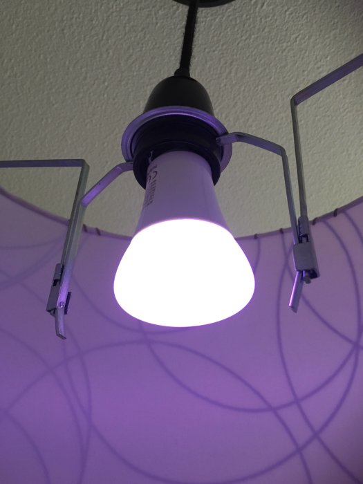 Nyinstallerad taklampa med tänd LED-glödlampa och porslinssockel synlig mot lila vägg.