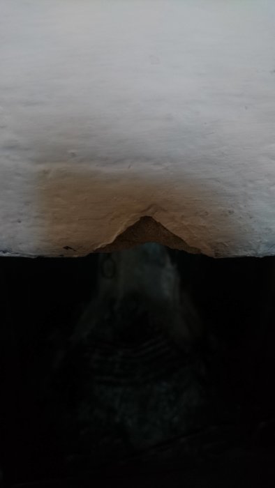 Ett skadat hörn på en öppen spis där puts har fallit av och exponerat teglet under.