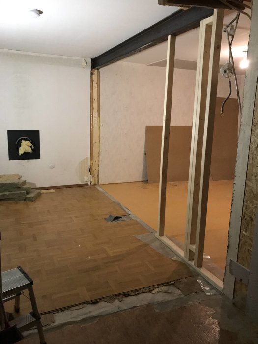 Nyinstallerad stålbalk i taket med trästöd och en delvis nedmonterad vägg för renovering i ett rum.