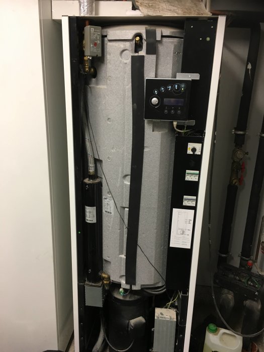 Öppen värmepump med synliga komponenter såsom ledningar, rör och kontrollpanel.