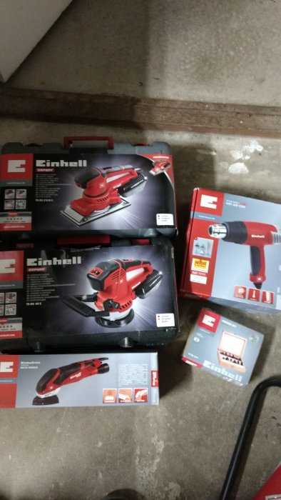Nyköpta Einhell verktyg, inklusive slipmaskin och varmluftspistol, i originalförpackningar på ett betonggolv.