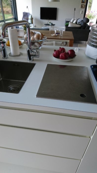 Modern kök med Bosch köksmaskin, diskho och skärbräda på vit bänkskiva.