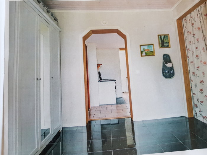 Interiörbild av en hall med öppen dörr, kakelgolv, en garderob och väggdekorationer.