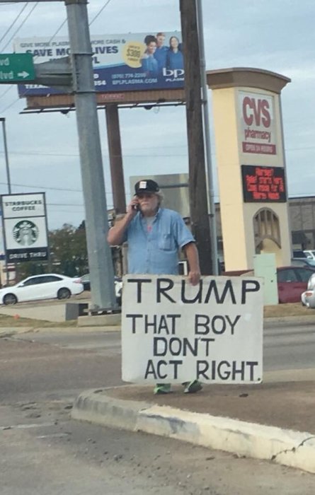 Person står vid vägkant med skylt med texten "TRUMP THAT BOY DONT ACT RIGHT.