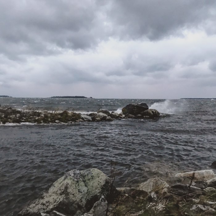 Mörk himmel och vågor som slår mot klippor på en blåsig kustlinje.