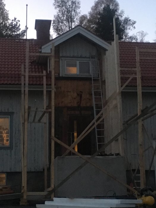 Plankställning framför hus under renovering i skymningen.