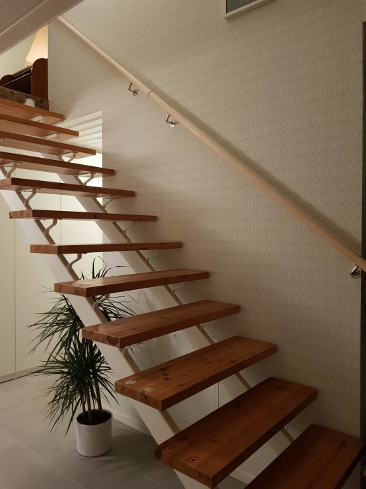 Nyinstallerad träledstång längs en modern trappa med öppna trästeg.