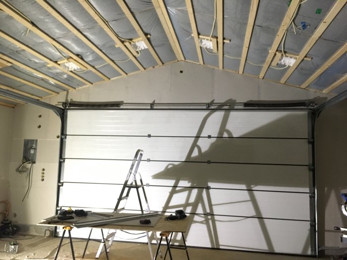 Renoverad garageinteriör med ny OSB och gips på taket, och en stege framför en stängd garageport.