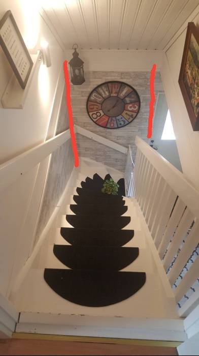 Interiörbild av en trappa med svarta steg, vita stolpar och väggar, med en stor klocka högst upp.