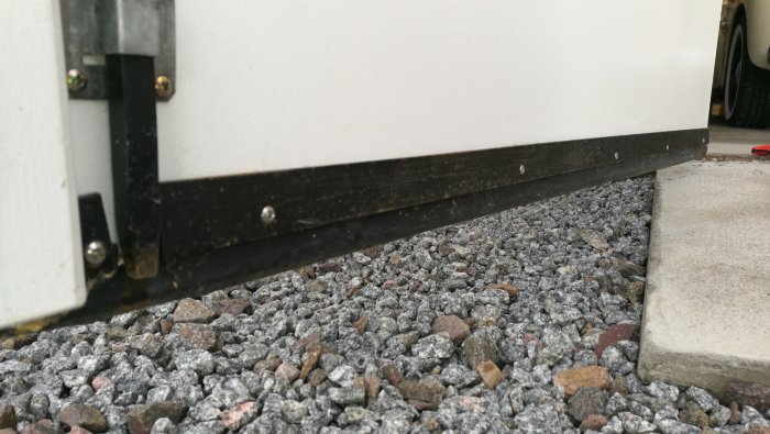 Närbild av en svart list monterad längs med en vit garagedörr och marken, klämd med plattjärn.