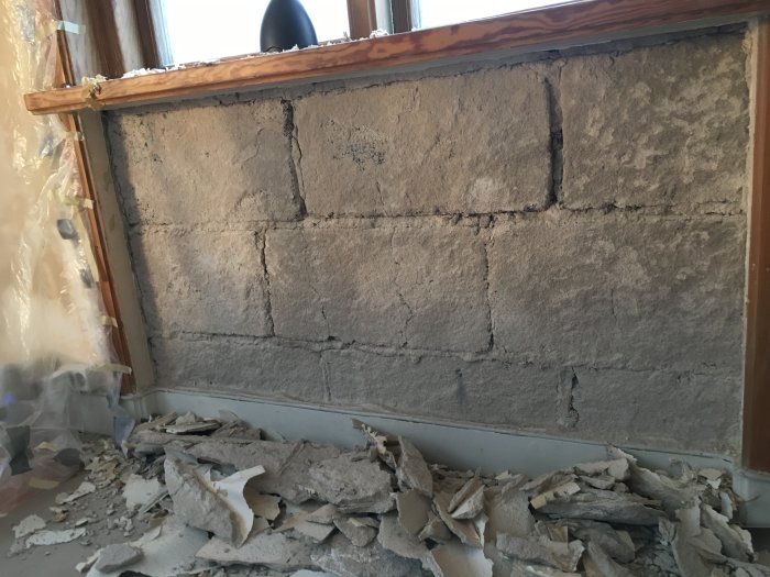 Avlägsnad strukturtapet och lös tapet som ligger i högar vid en bar betongvägg under ett fönster.