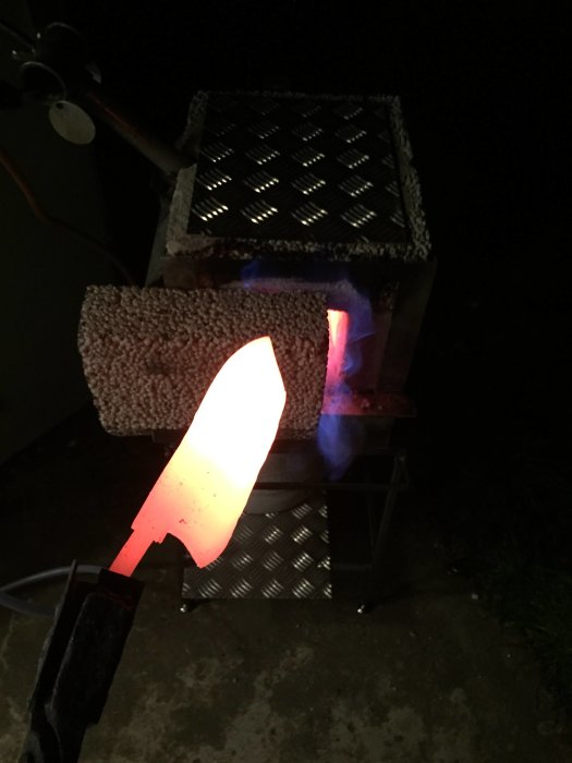 Uppgraderad ässja med glödande metallstycke i knivhållare, synlig låga och reglerventil i mörker.