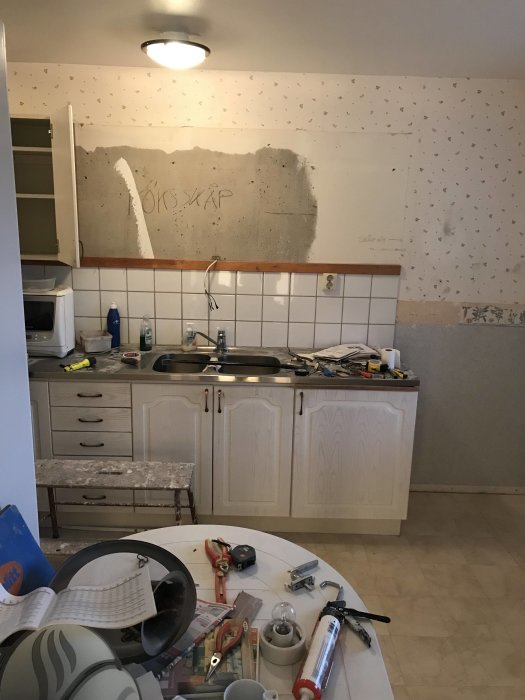 Kök under renovering med borttagna överskåp och verktyg utspridda på köksbänk och golv.