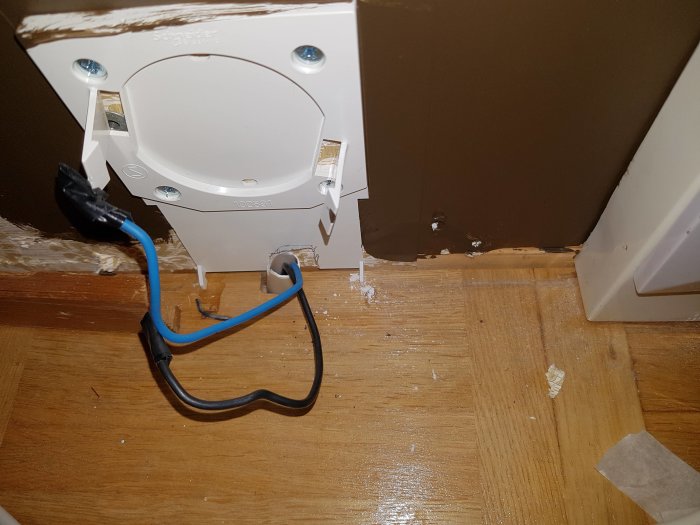 Eluttag utan frontplatta med synliga kablar vid sidan av en vägg och ett golv.