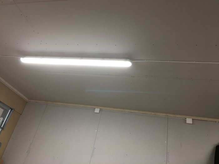 Tak med lysrörslampa och delvis monterade väggskivor i ett garage under renovering.