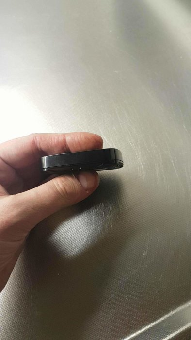 En hand håller en kompakt svart fuktsensor mot en metallisk yta.