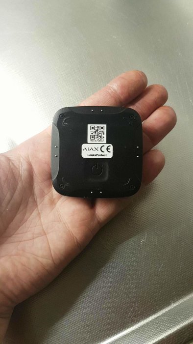 En hand håller en liten fuktsensor märkt med "Ajax LeaksProtect".