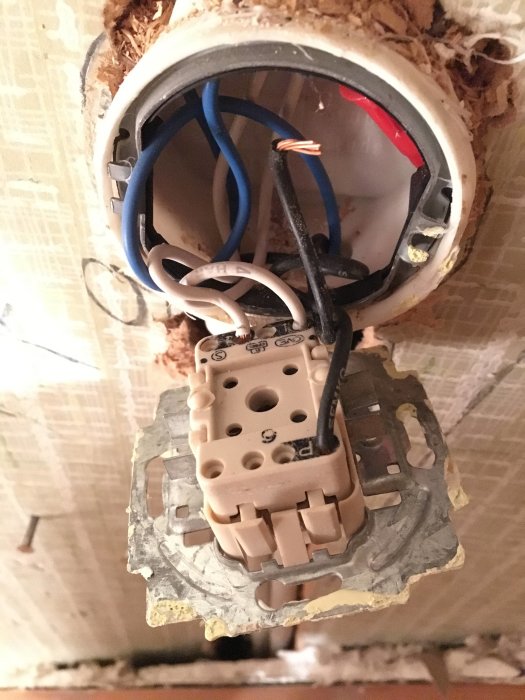 Öppen eldosa med en lös svart kabel och exponerad koppar vid en lampknapp i ett hus under renovering.