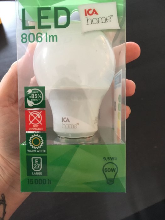 Hand som håller en LED-glödlampa i förpackning med texten "9,5W = 60W" och energibesparingsinformation.