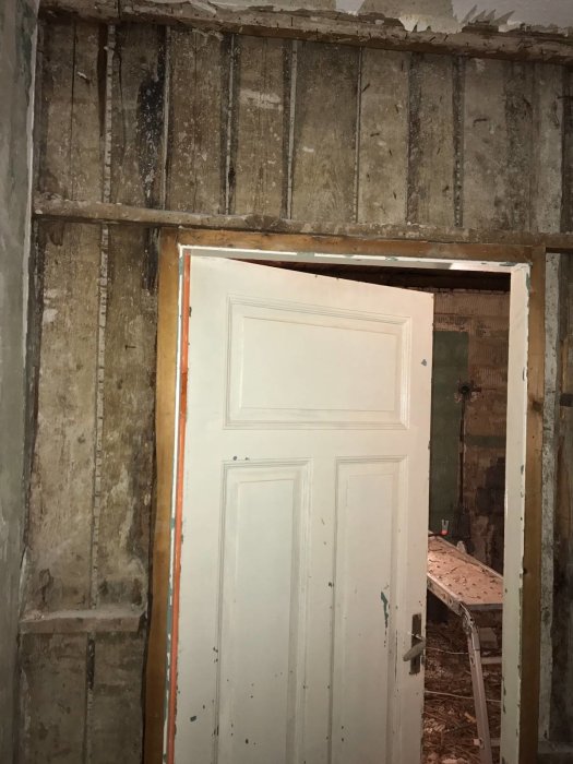 Gamla träväggar med exponerade stolpar och en delvis synlig dörrkarm i ett renoveringsprojekt.