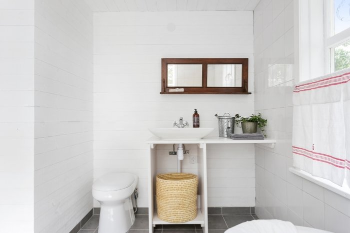 Ljust badrum med vita väggar, spegelfönster, handfat och toalett, inredd i minimalistisk stil.