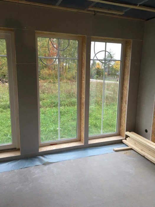 Inomhusvy av rum under renovering med osmyckade fönster och exponerad isolering.