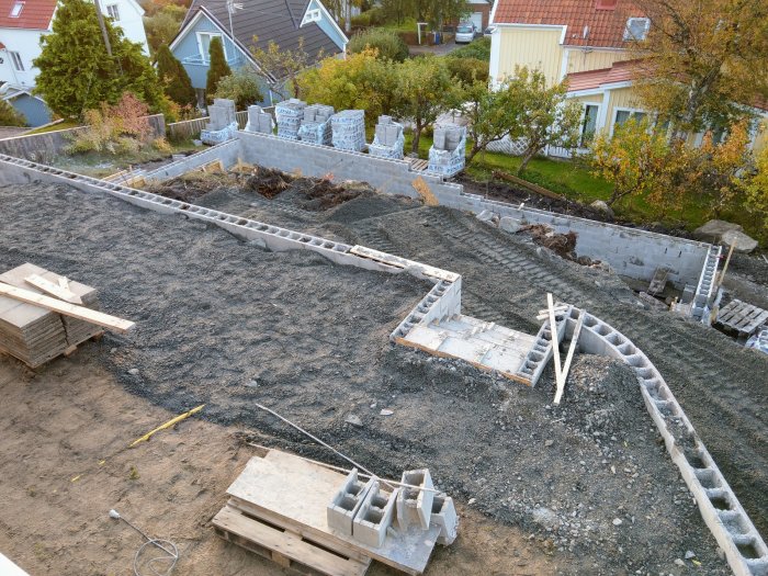 Grundarbete för ett hus med grus och betongblock, plus träformar för gjutning av grunder.