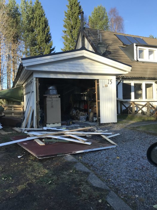 Husfasad under renovering med avrivna delar och bråte på marken framför öppet garage.