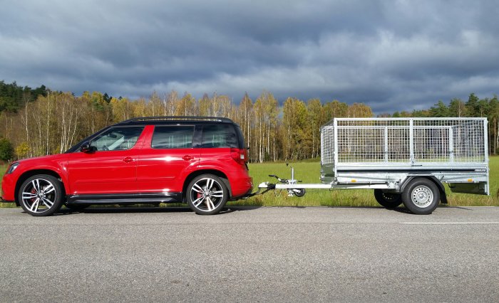 Röd VW Caddy parkerad bredvid en ny Fogelsta L1250 släpkärra på en väg med skog i bakgrunden.