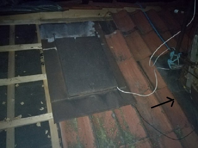 Mörk bild på ett tak med gamla enkupiga takpannor, en taklucka och en pil som pekar på ett icke-överlappande område.