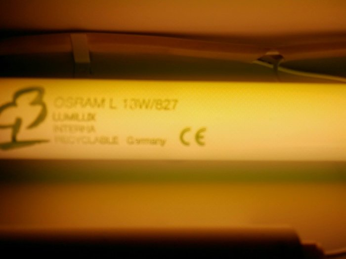Närbild på en tänd fluorescerande lampa med texten "OSRAM L 18W/827".