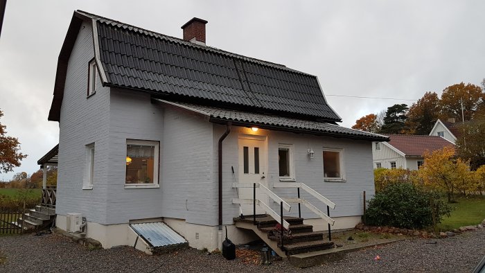 Vitmålat hus med svart tak och veranda som behöver renovering och plats för utbyggnad.